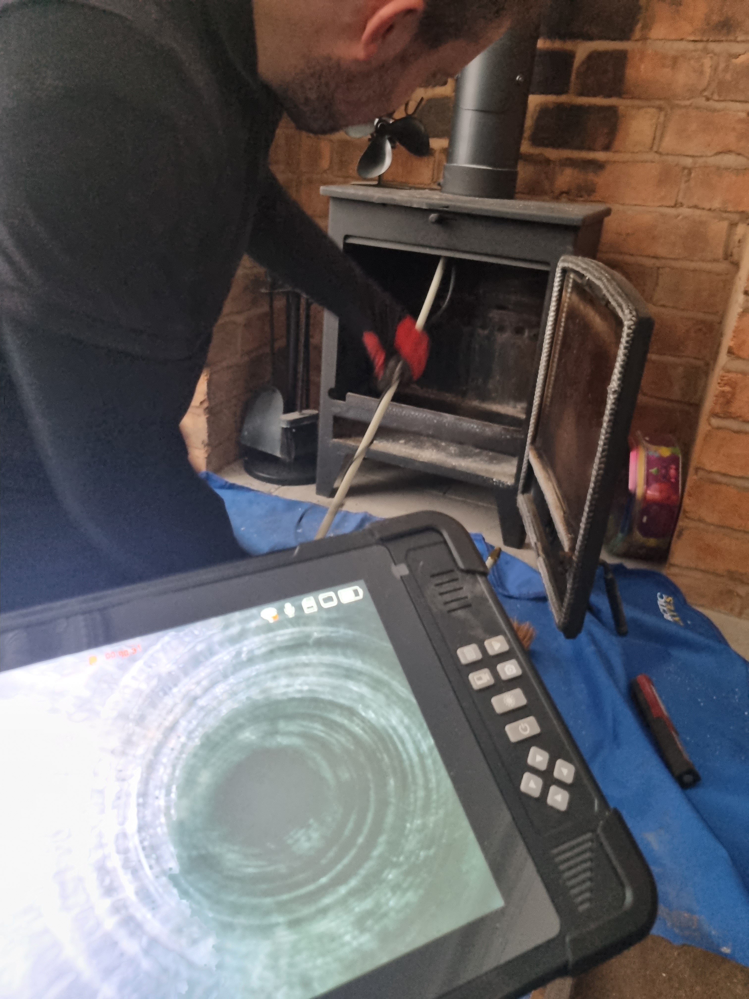 A technician using a tablet for CCTV inspection of a chimney while checking a stove, with tools and equipment visible around.
