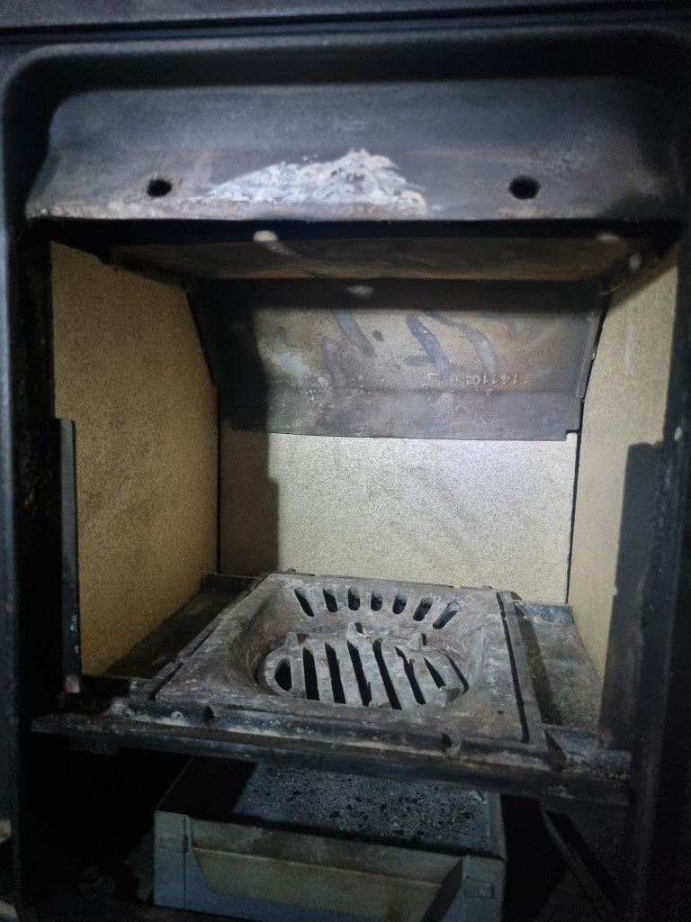 Interior view of a clean wood stove showing the grate and firebrick lining.